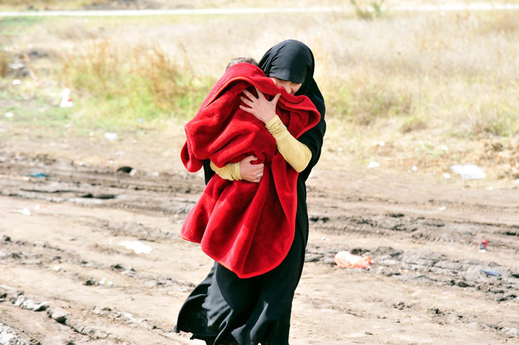 Mulher carrega uma criança debaixo de um cobertor ao sul da cidade sérvia de Presevo. Foto: UNICEF/Tomislav Georgiev