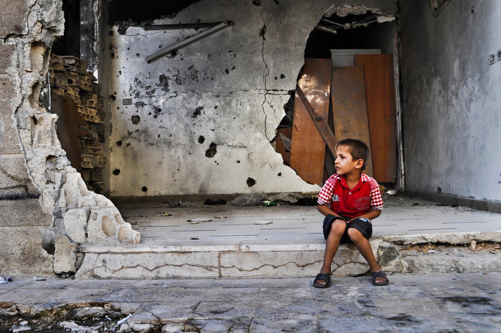 Menino em frente a um edifício destruído na cidade de Homs, Síria. Foto: PMA/Abeer Etefa