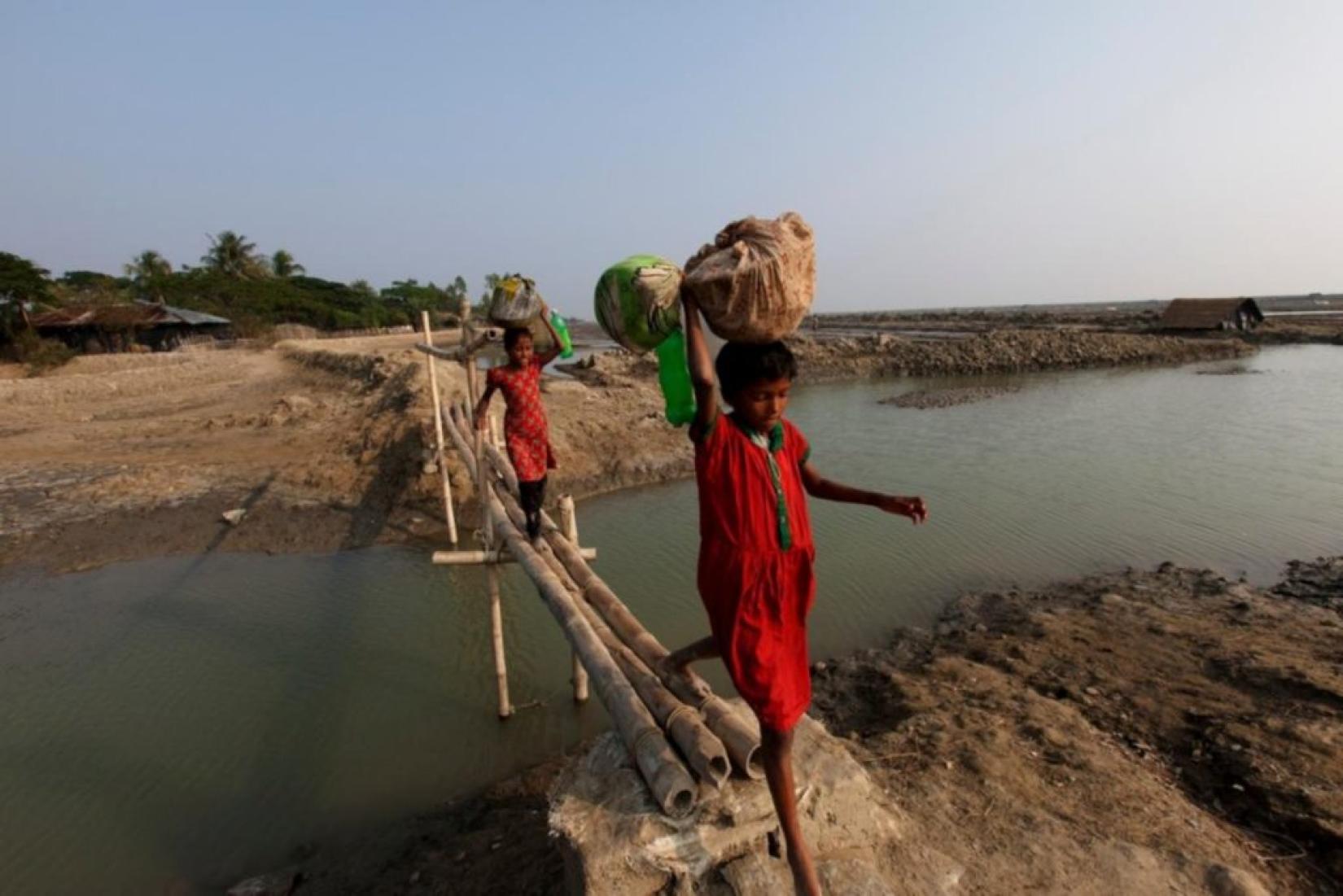 Meninas atravessam ponte de bambu na ilha de Katubidia em Bangladesh, onde milhões de pessoas estão em risco devido ao aumento do nível do mar. Foto: ACNUR / Saiful Huq Omi.