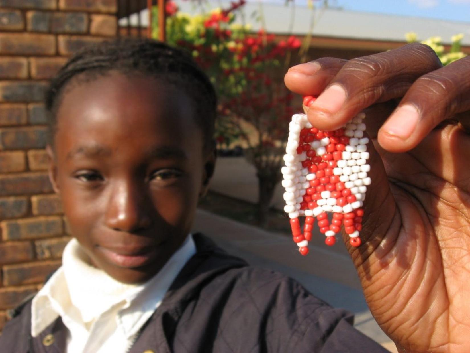 Jovem sul-africana exibe miçanga com o símbolo do movimento pelo fim da AIDS. Foto: Peace Corps/PEPFAR