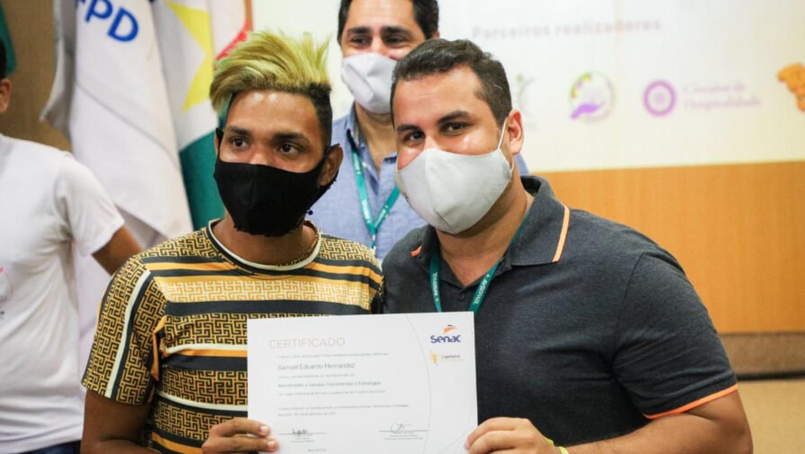 Valentina (esquerda) recebe seu diploma, após 80 horas de formação, das mãos de um profissional da organização AVSI, parceira do ACNUR em Boa Vista. 