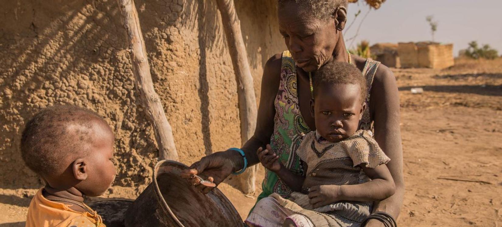 Uma mãe dando mingau para seus filhos. Um número crescente de crianças no norte de Bahr el Ghazal e Warrap, no Sudão do Sul, faz apenas uma refeição por dia.