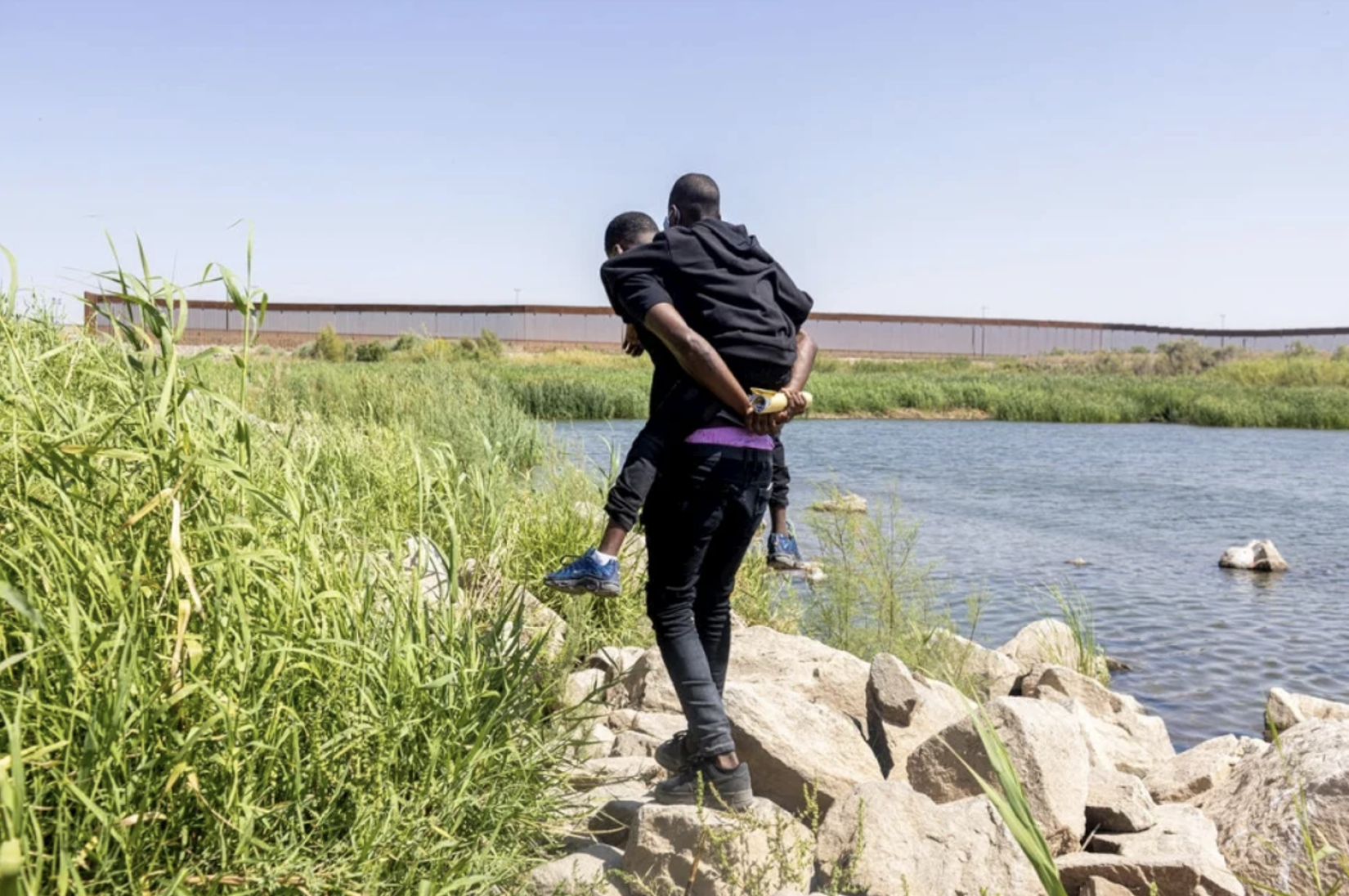 Homem haitiano carrega seu filho através da fronteira entre o México e os Estados Unidos para solicitar asilo.