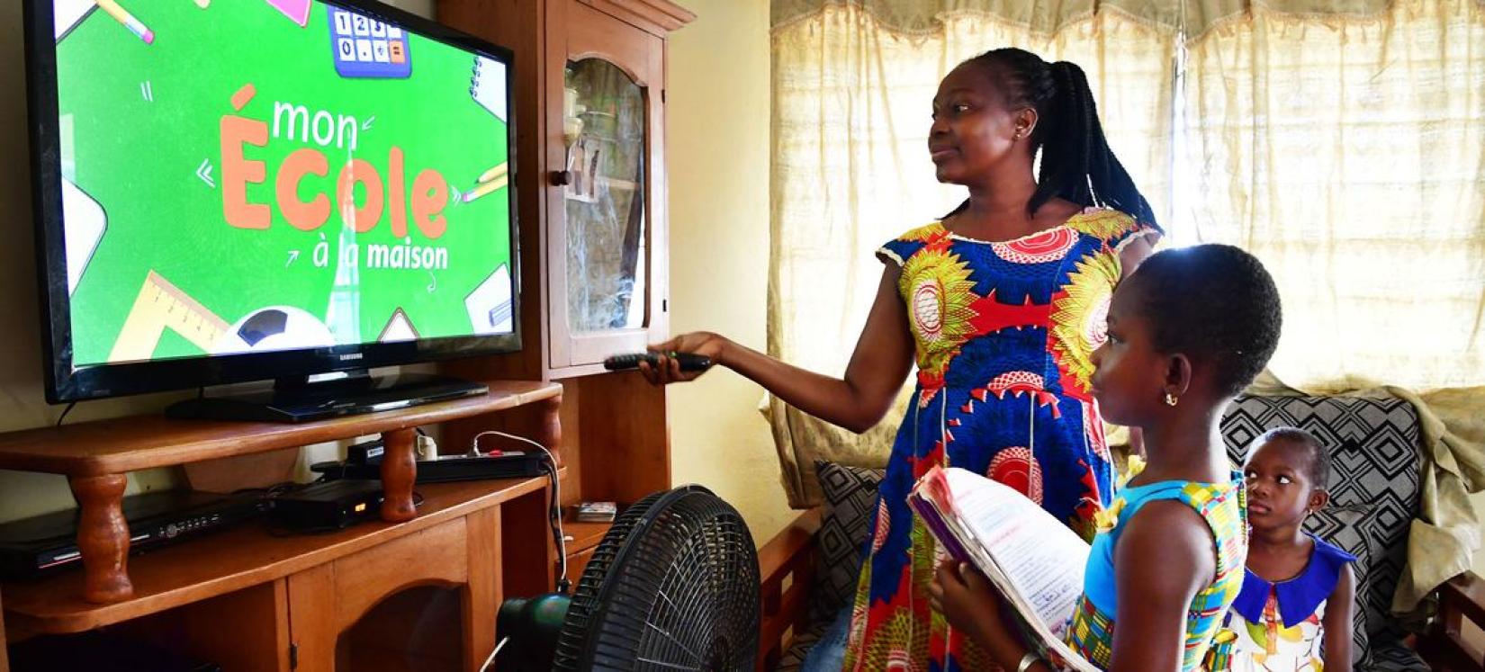 Uma mãe ajuda sua filha de oito anos a ter aulas na televisão durante a pandemia de COVID-19 em casa em Man, Costa do Marfim.