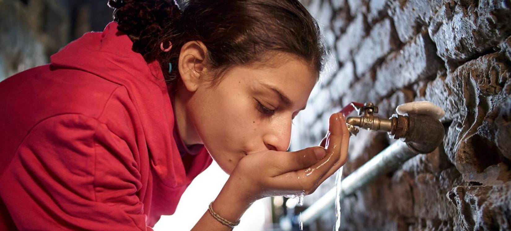 Uma menina bebe água de uma torneira em sua casa na cidade do Cairo, no Egito