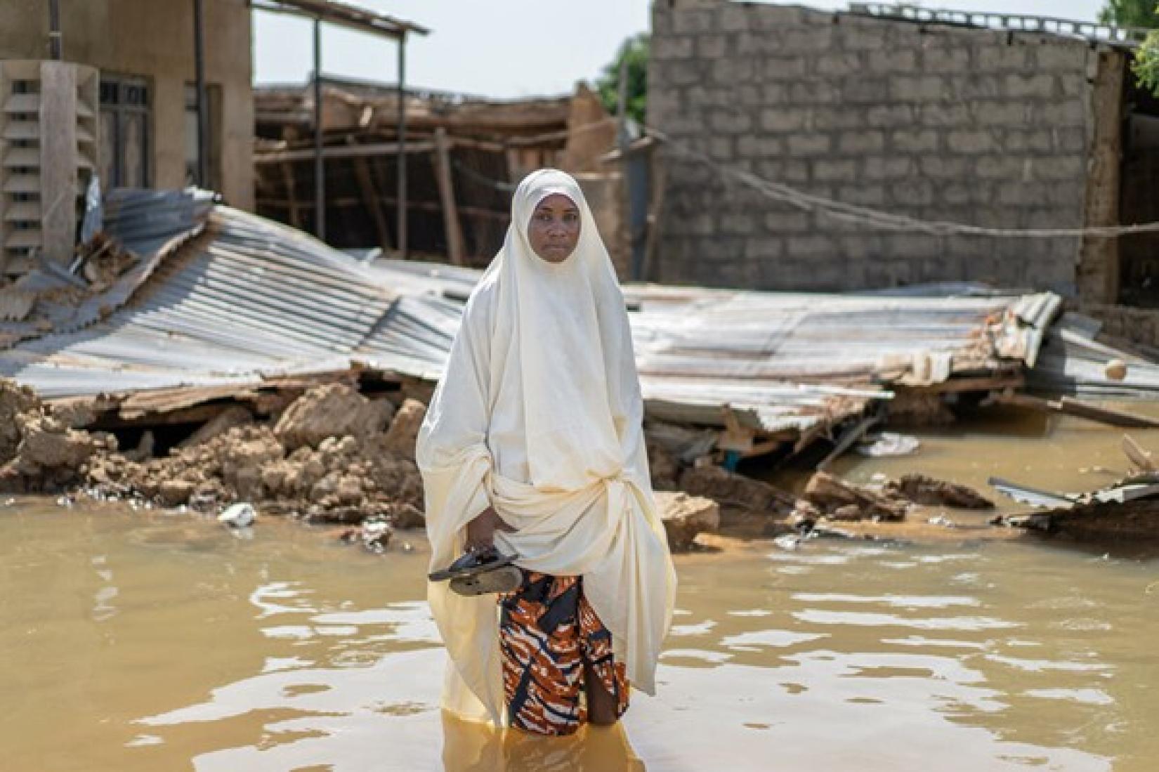 Huawa, de 37 anos, na frente de sua casa em Gigir, na Nigéria, destruída por inundações em outubro – eventos climáticos extremos destroem plantações e interrompem o acesso das pessoas à comida. 