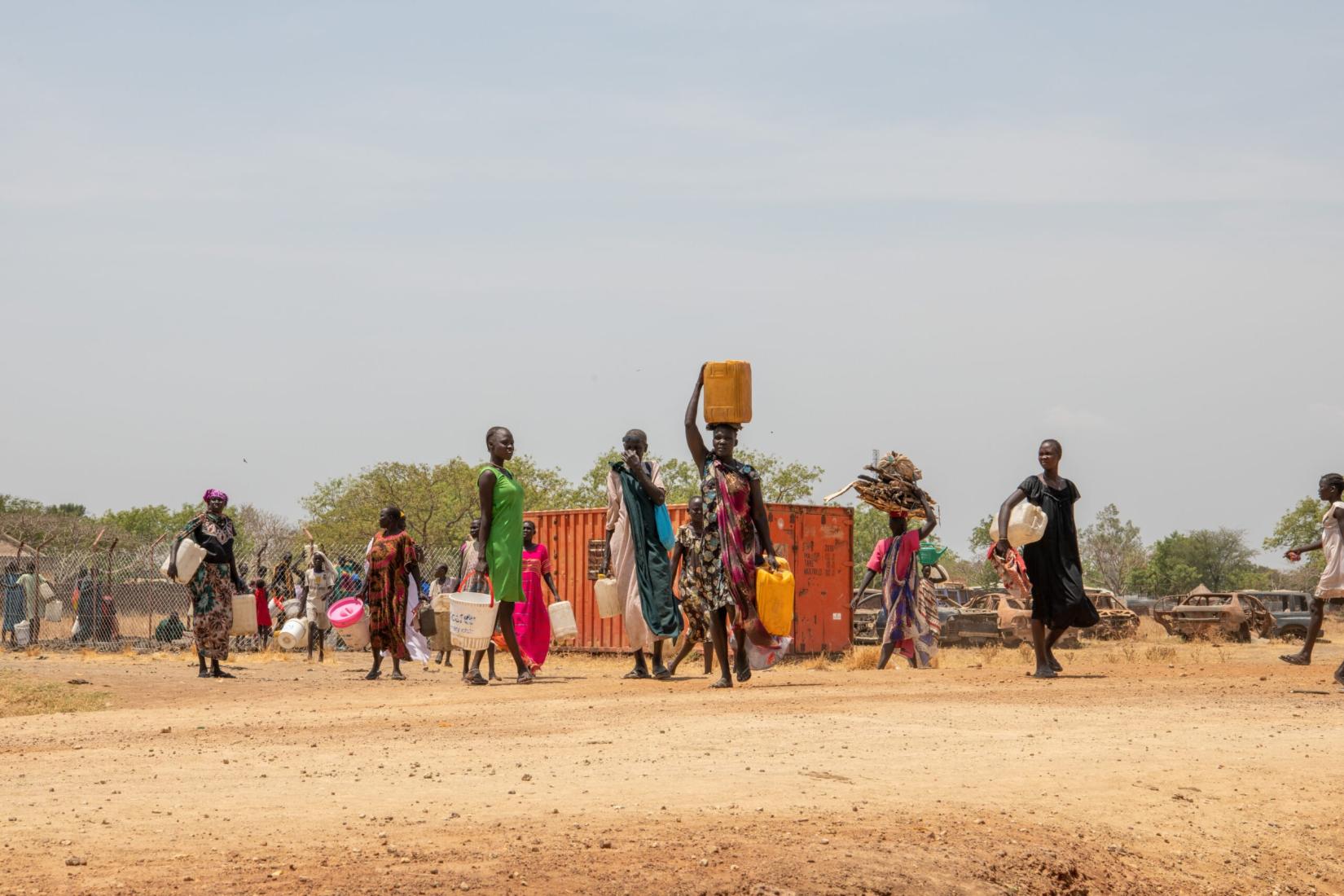 Mulheres sul-sudanesas retornam para suas casas com barris vazios após a fonte de água que compartilhavam secar.