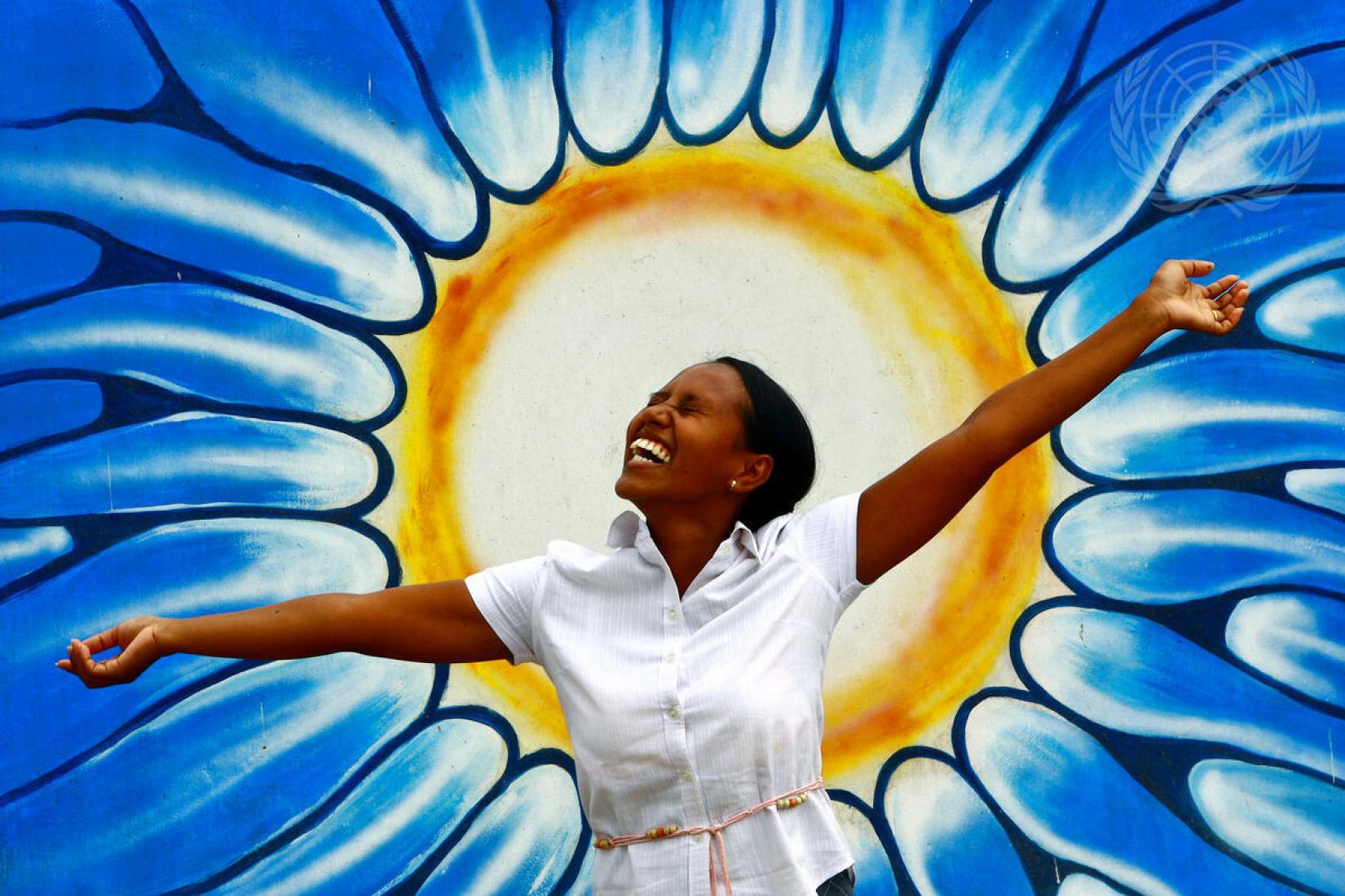 Uma mulher posa em frente a um grafite representando o sol por ocasião da comemoração do Dia Mundial da Saúde Mental.