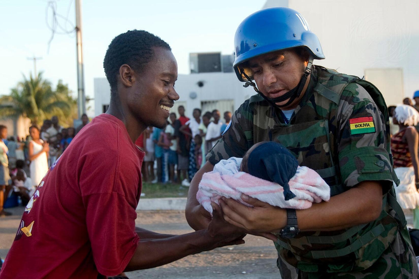 Um pacificador boliviano da ONU entrega um bebê ao seu pai durante a distribuição de água e refeições aos moradores de Cité Soleil, no Haiti. Foto ONU/Marco Dormino