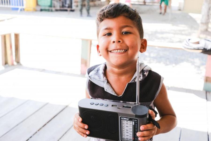 José Andrés Romero Osorio, de 3 anos, contente com o aparelho de rádio distribuído para ele e sua família para acompanhar o programa Súper Panas na Rádio, no abrigo Rondon 2, Boa Vista (RR).
