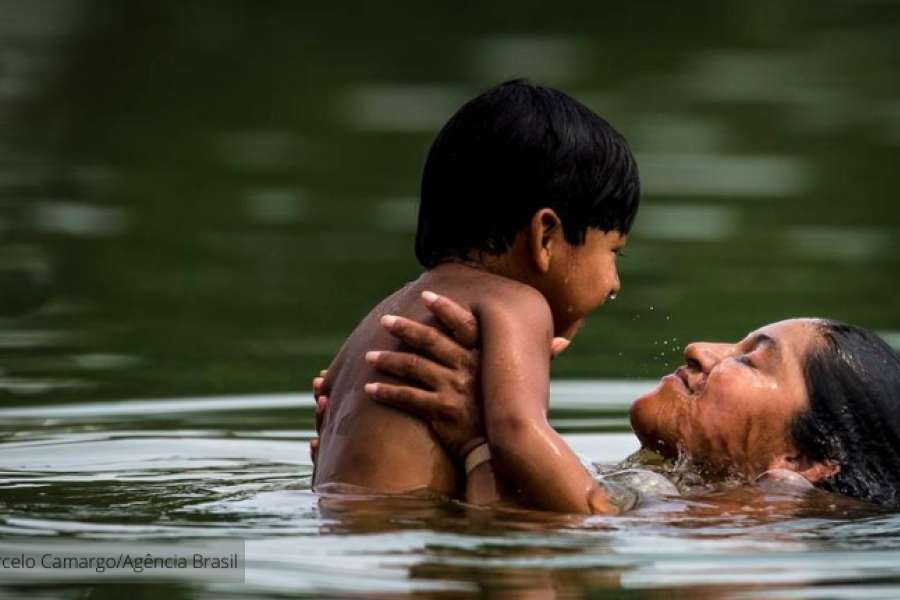mulher indígena brinca na água com criança