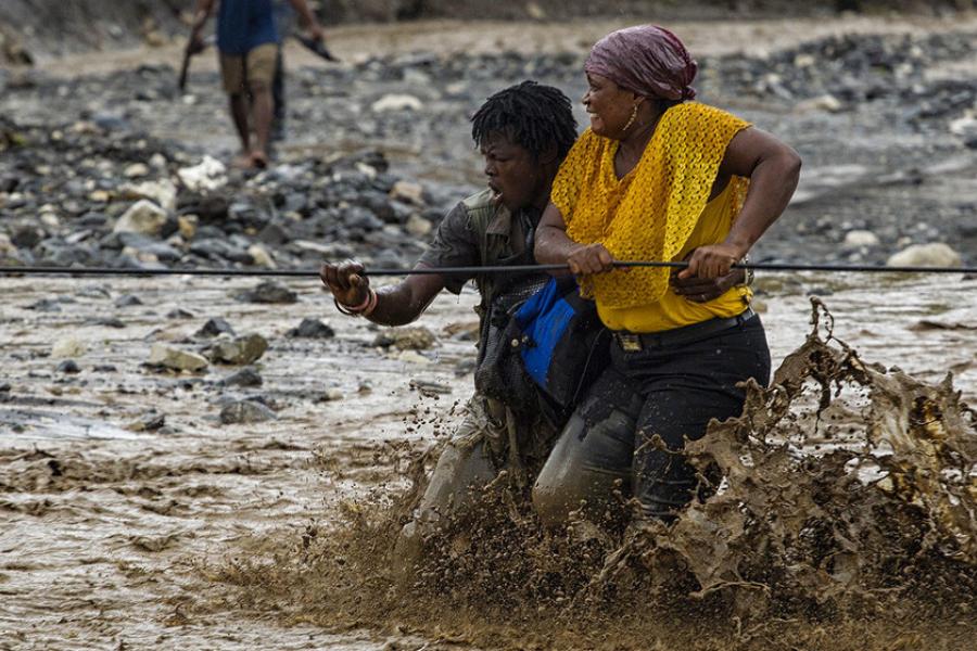 Pessoas atravessam um rio inundado no oeste do Haiti depois que uma ponte foi destruída pelo furacão Matthew