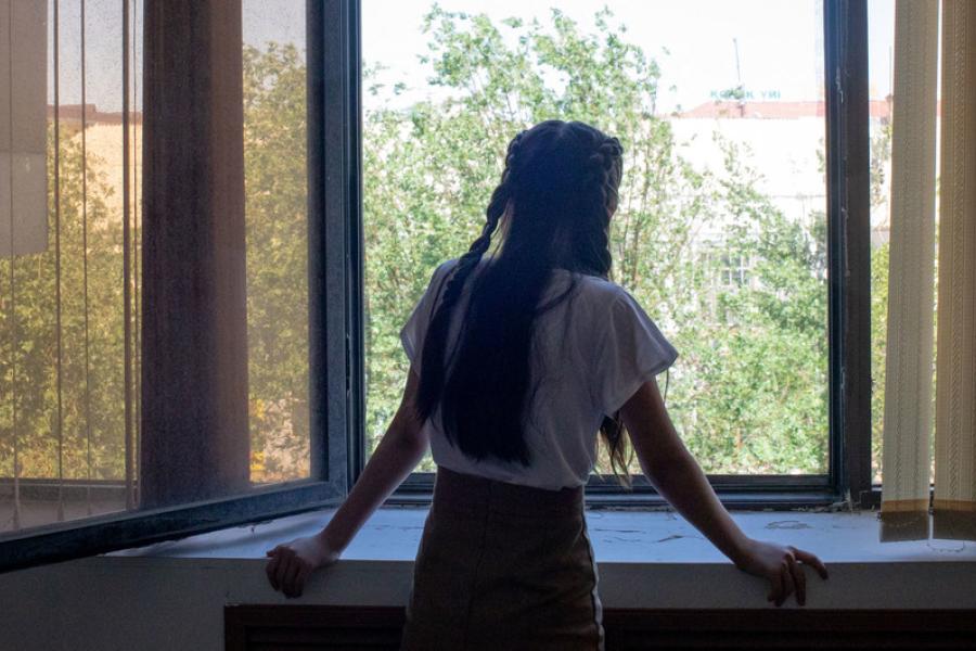Uma menina de 14 anos olha pela janela, em Kyzylorda, no Cazaquistão. Recentemente, ela trabalhou sentimentos de estresse e ansiedade com um psicólogo educacional