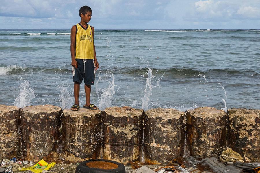  Um menino está em um paredão que protege a casa de sua família da elevação do mar no Atol de Majuro, nas Ilhas Marshall