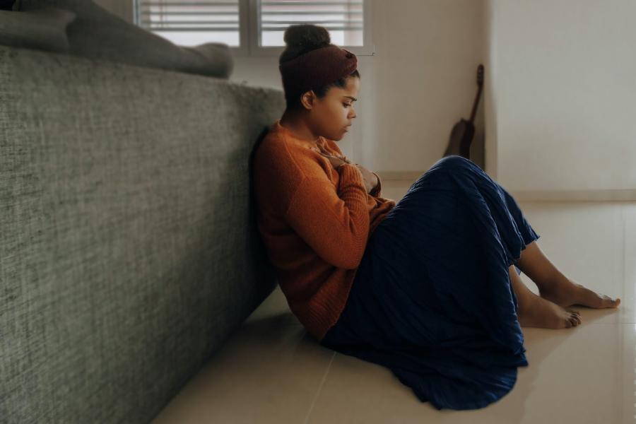 mulher negra está sentada com a mão no peito e as costas apoiadas em um sofá