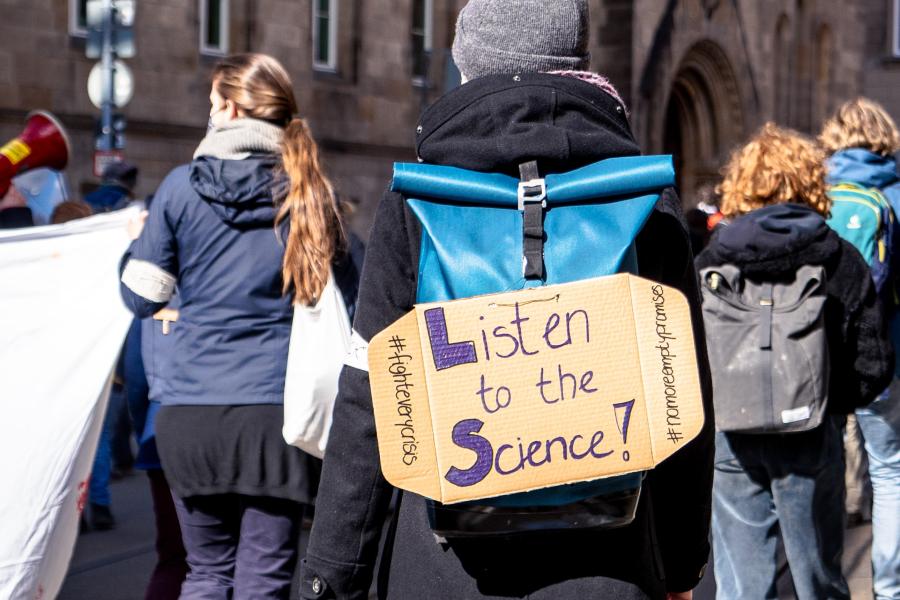 estudante leva um cartaz nas costas em que se lê: escute a ciência