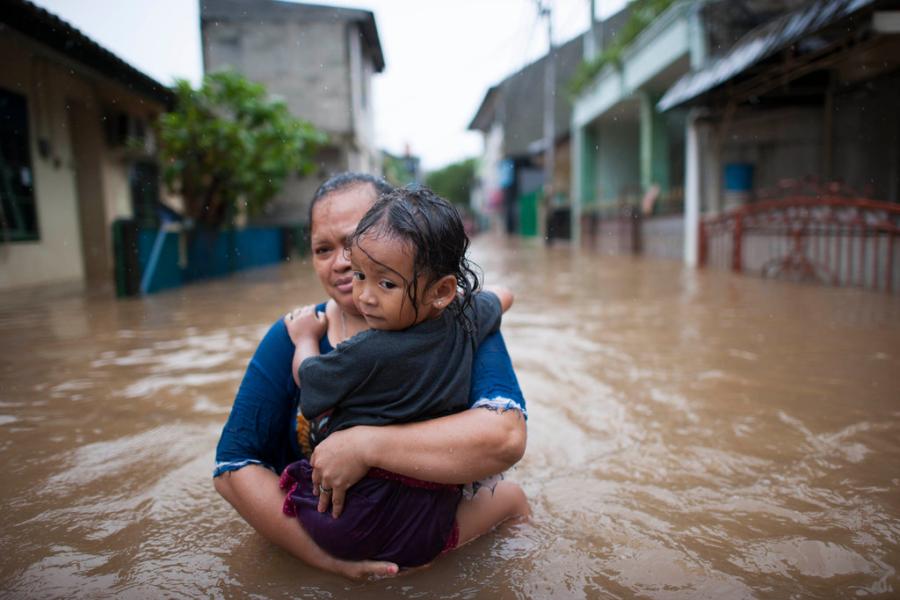 Mulher e criança caminham pelas águas da enchente no leste de Jacarta, Indonésia