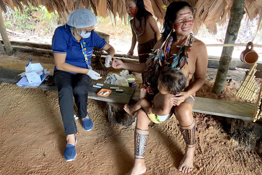 uma mulher indígena recebe atendimento de saúde com seu bebê no colo