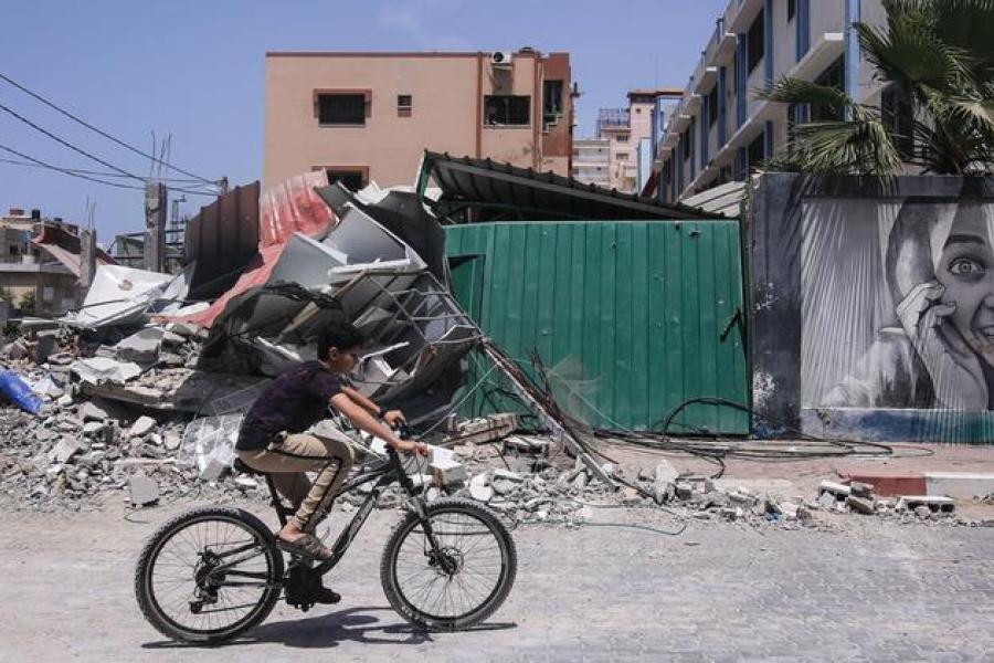 Um menino anda de bicicleta ao lado de prédios destruídos após ataques israelenses na Faixa de Gaza, Palestina