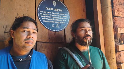 Os irmãos André Augusto Vilar Martim e Anderson Augusto Vilar Martim, agentes de saneamento na Terra Indígena Jaraguá Kwaray Djekupe, diante da placa dedicada à avó, a Cacica Jandira. 